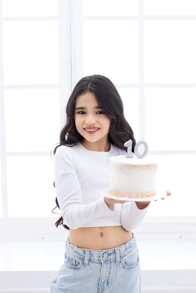 Niña sonriente con una torta de cumpleaños en un estudio blanco